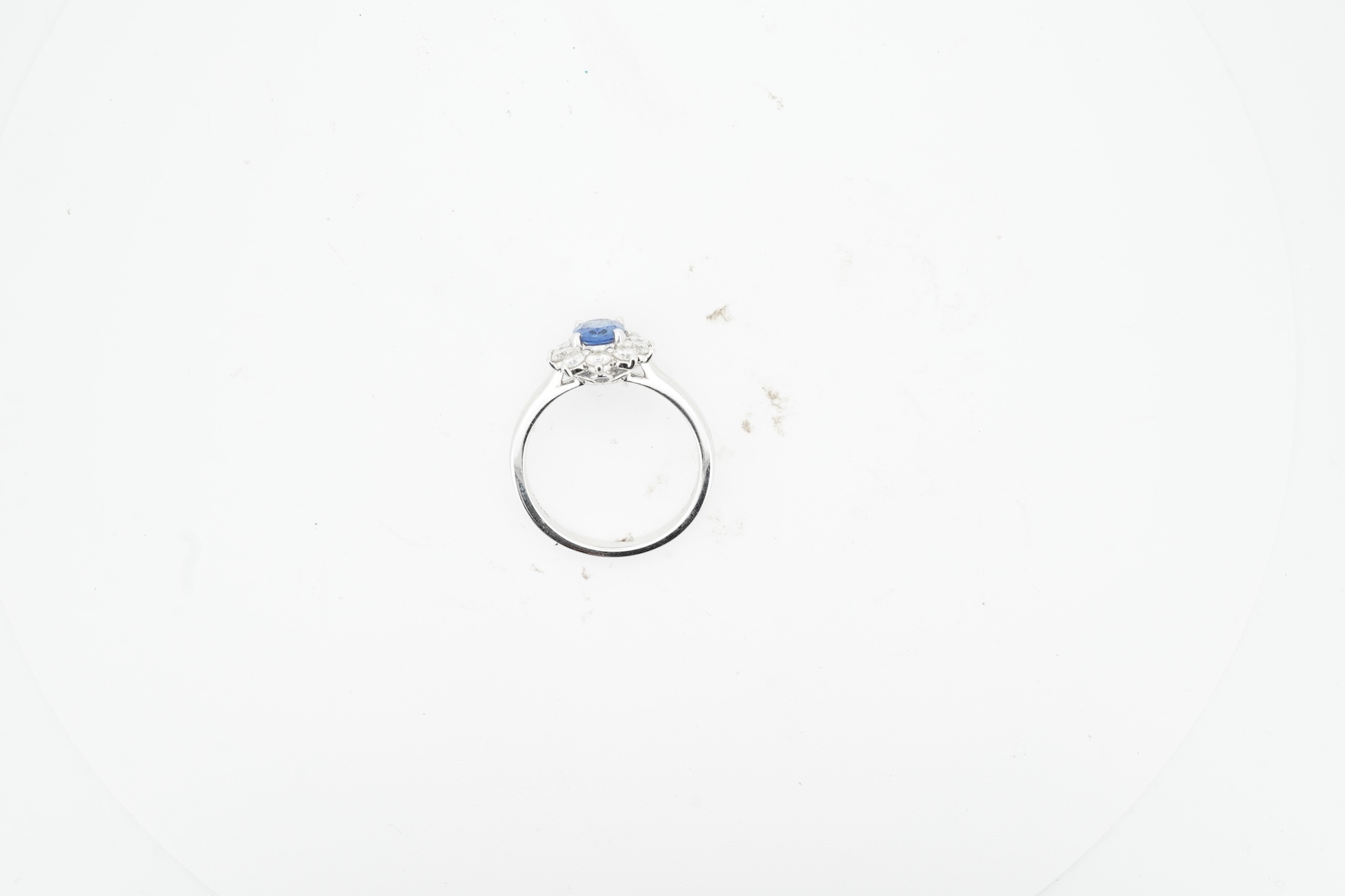 A sapphire and diamond cluster ring, claw-set with an oval sapphire weighing approximately 0.77 carats, within a border of brilliant-cut diamonds totalling approximately 0.50 carats, mounted in white gold, size M, stampe